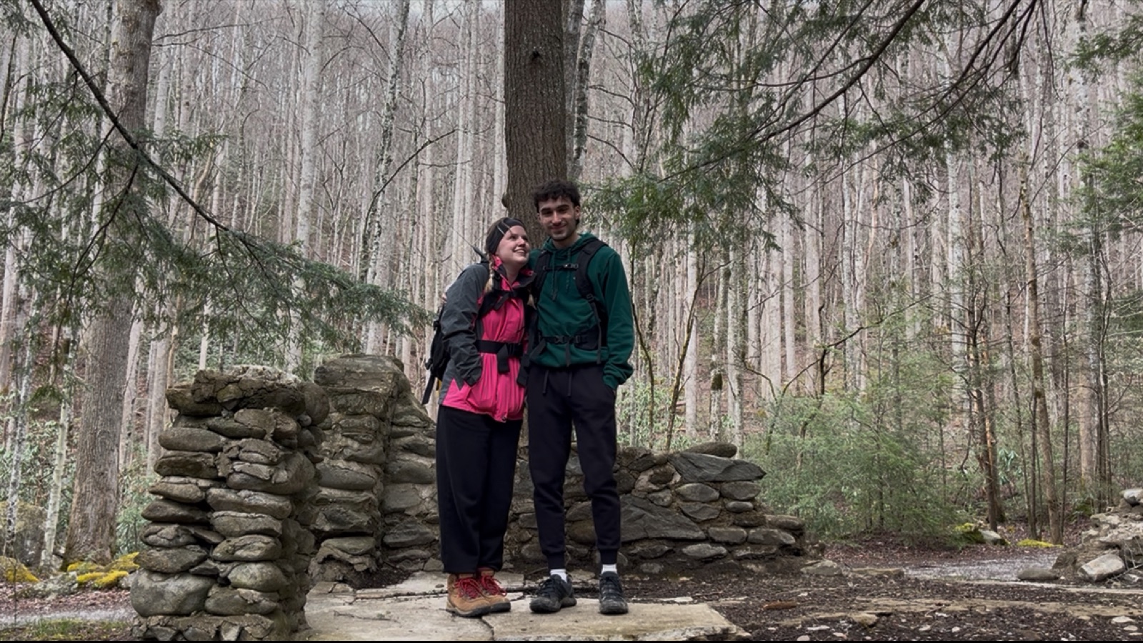 Maddox Schmidlkofer and his girlfriend standing together on a stone trail shelter in a misty, bare winter forest.